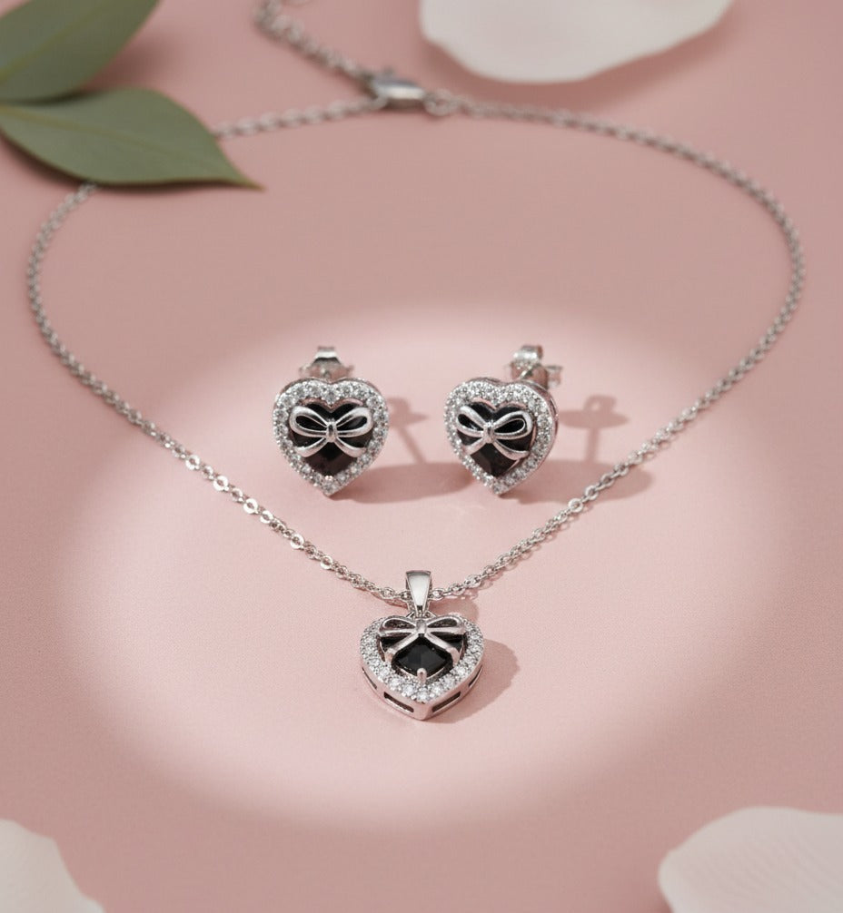 Silver heart-shaped jewelry set with necklace and earrings on a pink background