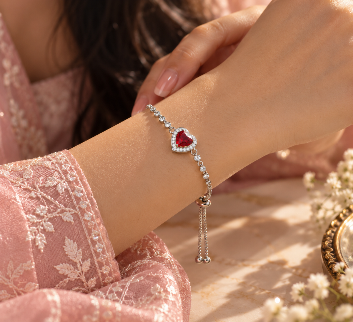 A close-up lifestyle shot of a delicate silver-toned Amour heart slider bracelet , worn on a woman's wrist. The bracelet features a dangling double-bead charm.