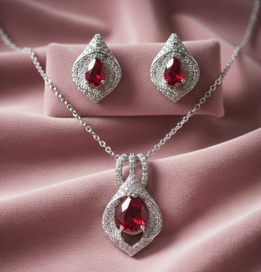 Jewelry set with red gemstones and silver accents on a pink fabric background