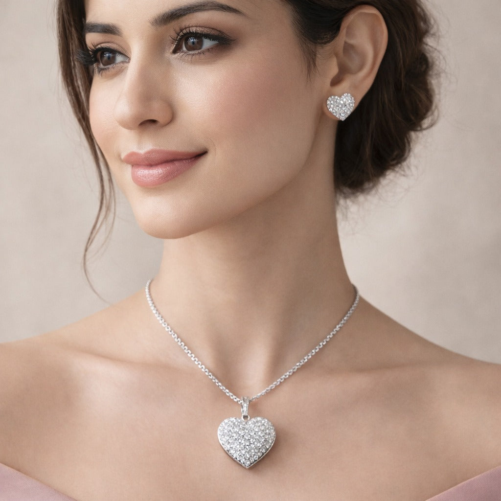 Woman wearing a silver heart-shaped necklace and earrings against a neutral background