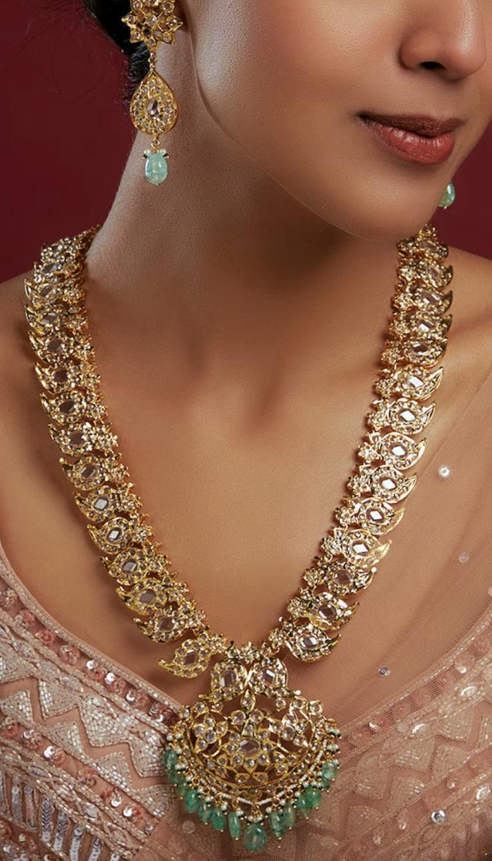 Woman wearing a gold necklace with green gemstones and matching earrings on a red background